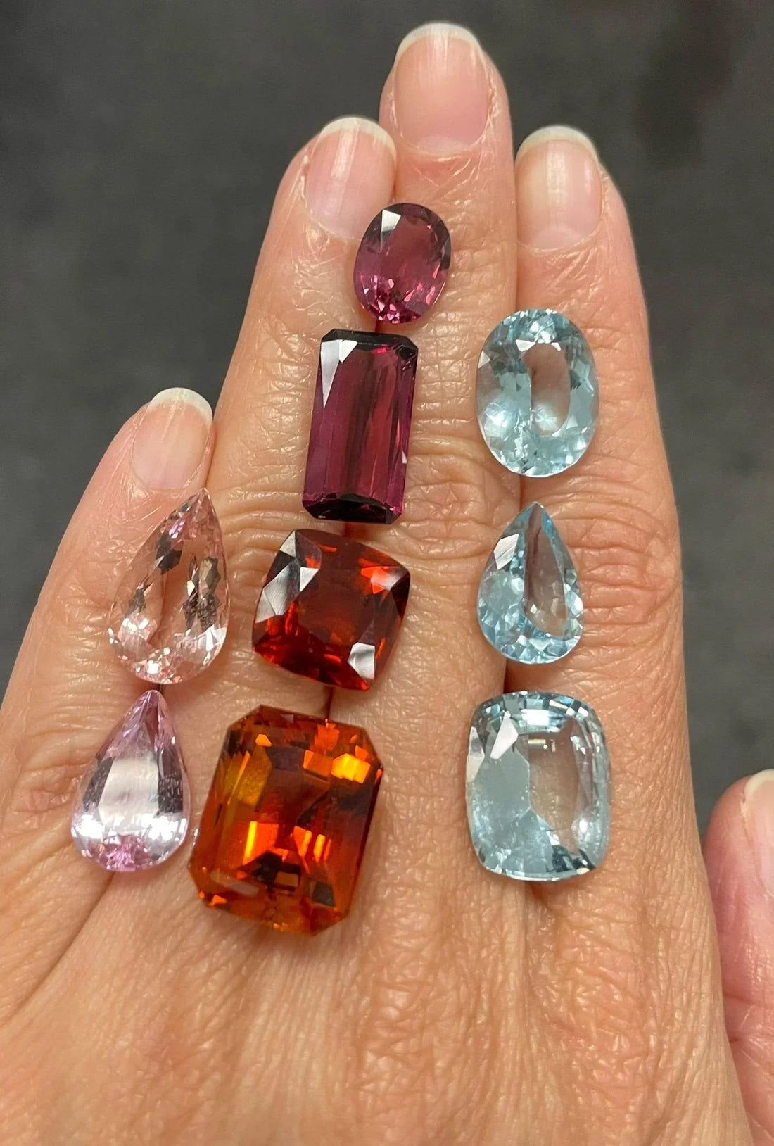 A hand with a selection of loose gemstones laid out of different sizes and colours