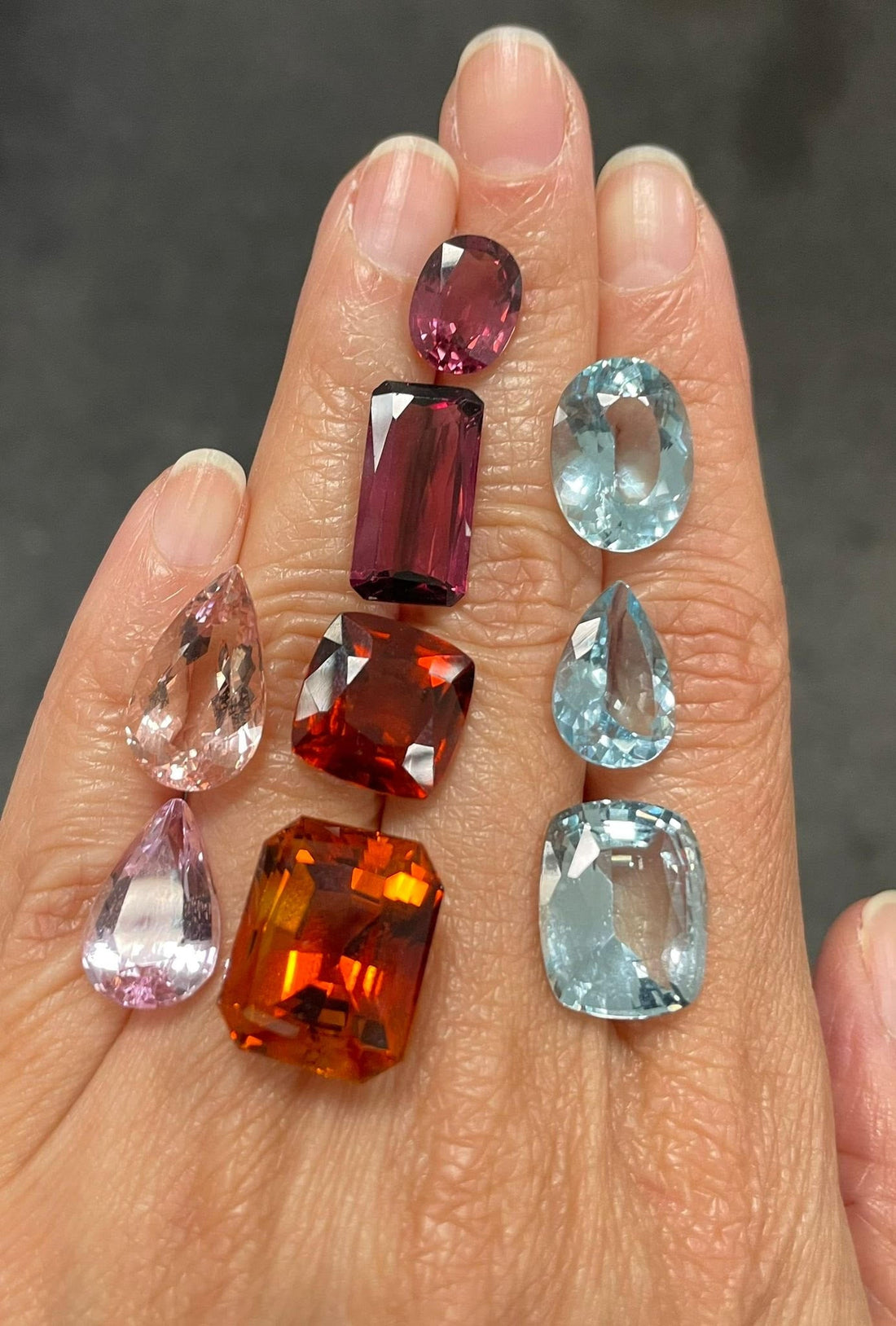 A hand with a selection of loose gemstones laid out of different sizes and colours