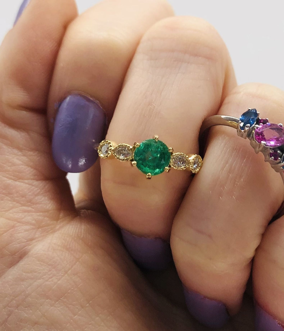 My hand holding the Milena emerald and diamond engagement ring and the Atlantis set with pink and blue sapphires.