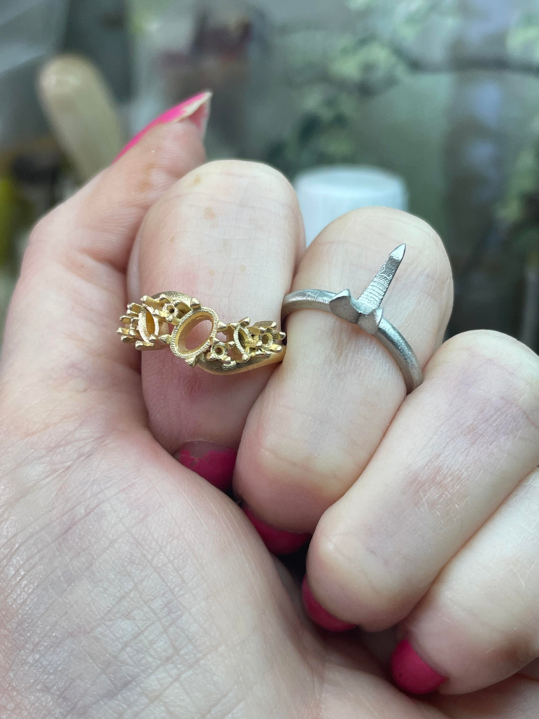 Two cast rings held on a hand — a yellow gold sculptural ring and a platinum ring — showing the colour and weight difference between the two metals, made in the Nude Jewellery London studio