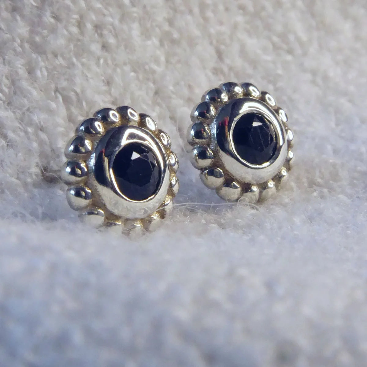 Pair of sterling silver stud earrings featuring faceted black spinel gemstones with a millgrain beaded border. 