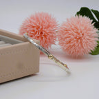 A silver and gold bracelet on a white surface with pink flowers and a jewellery box in the background.