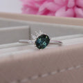 Selene oval teal sapphire and diamond asymmetric cluster engagement ring in 18ct white gold, presented in ring box showing the deep teal sapphire and diamond cluster, handmade in our London studio