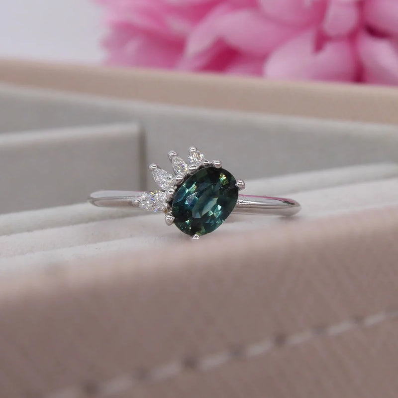 Selene oval teal sapphire and diamond asymmetric cluster engagement ring in 18ct white gold, presented in ring box showing the deep teal sapphire and diamond cluster, handmade in our London studio