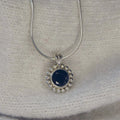 Alto Majestic black spinel and recycled silver pendant resting on a cream knit fabric, front view showing deep inky stone and millgrain beaded border on a snake chain