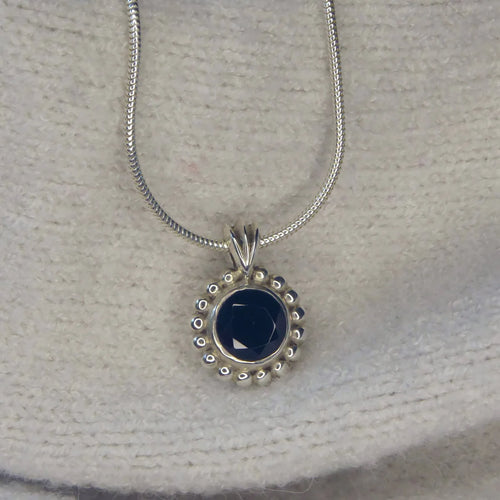 Alto Majestic black spinel and recycled silver pendant resting on a cream knit fabric, front view showing deep inky stone and millgrain beaded border on a snake chain