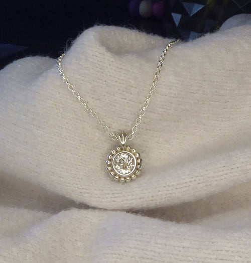 Silver necklace with a round pendant with white topaz on a white fabric background