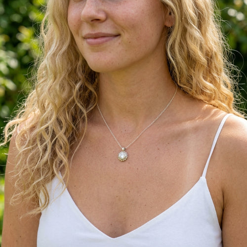 Model wearing the Alto Majestic pendant, featuring a clear, sparkling round white topaz gemstone set within a high-polished recycled silver geometric frame.