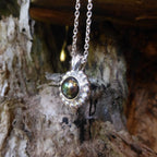 A side profile shot of the silver Alto Black Pearl pendant on a wooden surface     
