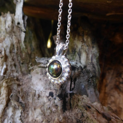 A side profile shot of the silver Alto Black Pearl pendant on a wooden surface     