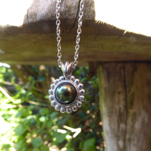 A front-facing view of the Alto Pearl pendant, featuring a round black freshwater pearl with peacock undertones set within a high-polished recycled silver geometric frame.