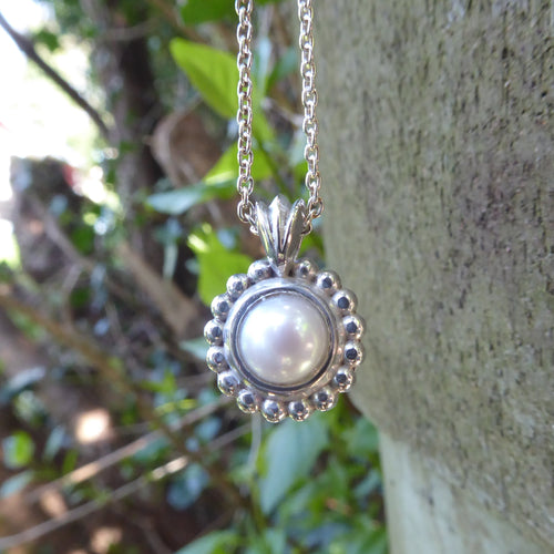 Pearl and silver necklace on a wooden surface with greenery in the background