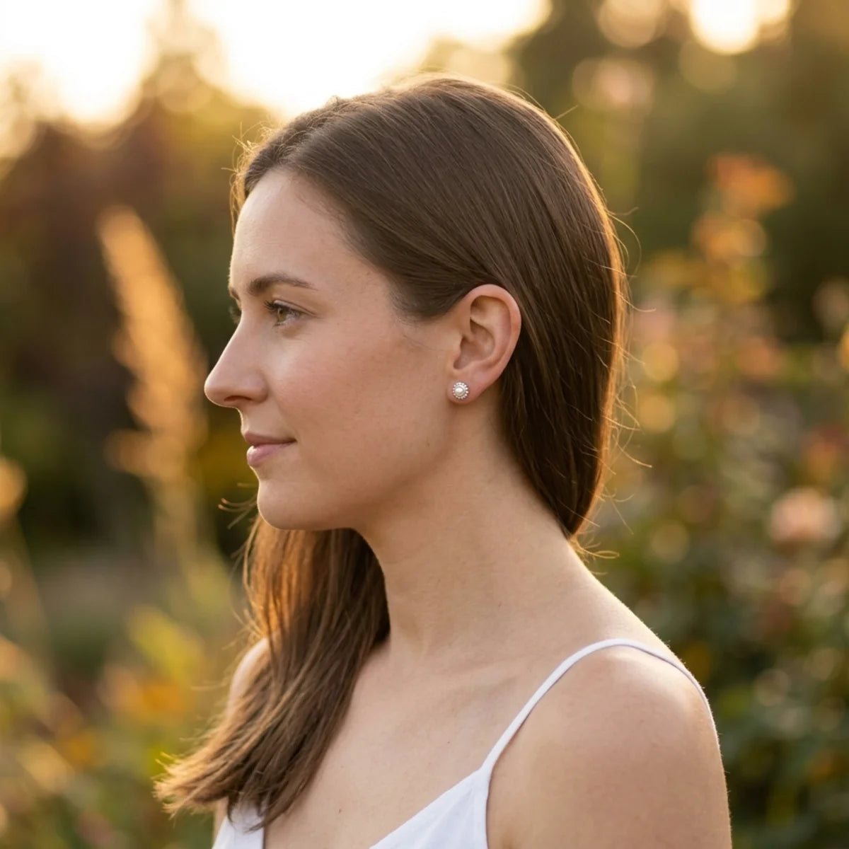 Ivory pearl and silver Mini Alto stud earrings worn by a model, shown in profile against a soft garden backdrop 