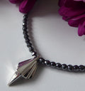 Art Deco sterling silver geometric pendant on faceted hematite bead necklace, close-up detail with magenta flowers