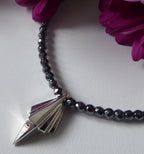 Art Deco sterling silver geometric pendant on faceted hematite bead necklace, close-up detail with magenta flowers