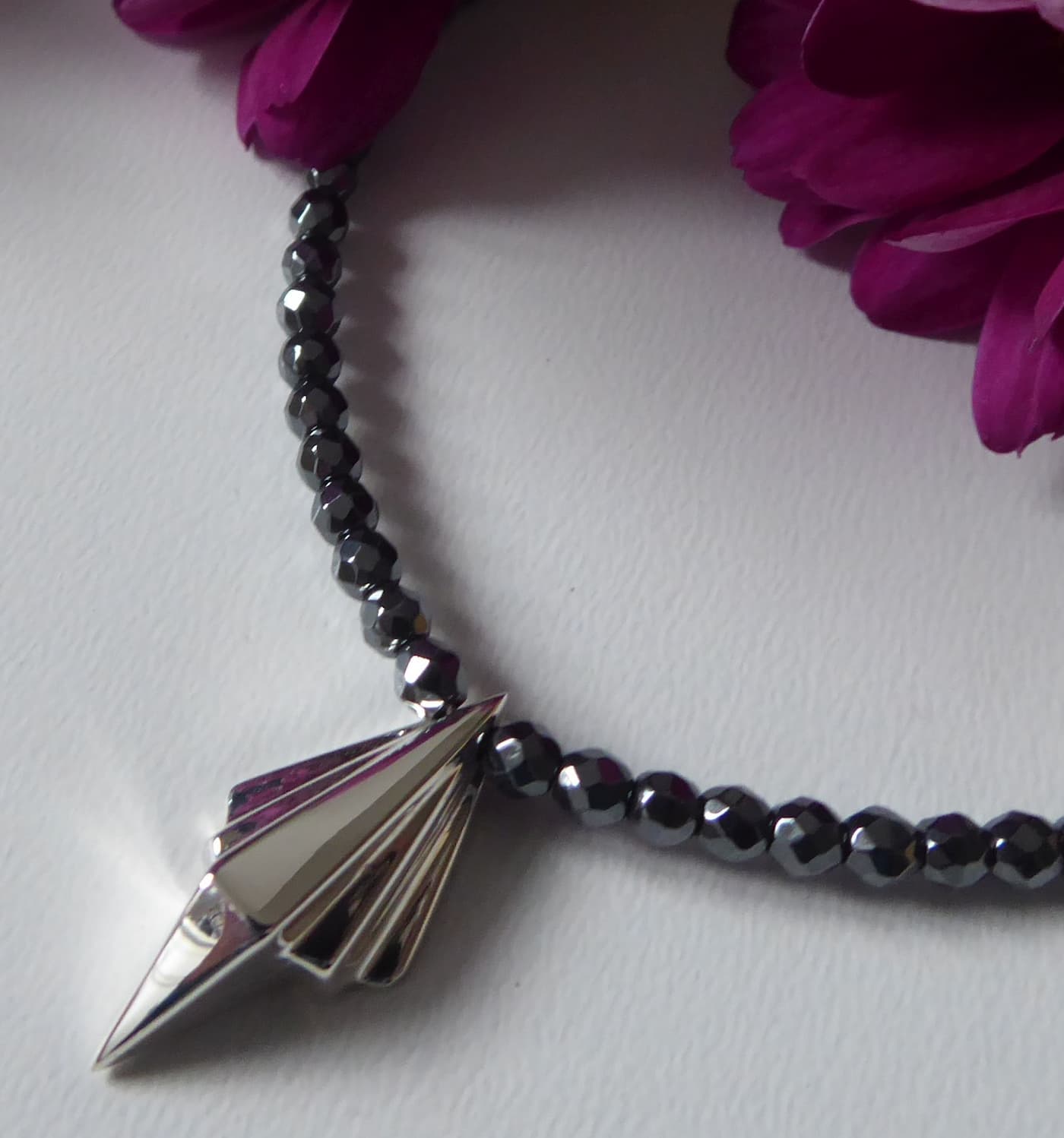 Art Deco sterling silver geometric pendant on faceted hematite bead necklace, close-up detail with magenta flowers