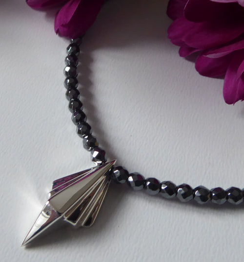 Art Deco sterling silver geometric pendant on faceted hematite bead necklace, close-up detail with magenta flowers