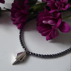 Full length Art Deco sterling silver geometric pendant on faceted hematite bead necklace, flatlay with magenta chrysanthemums