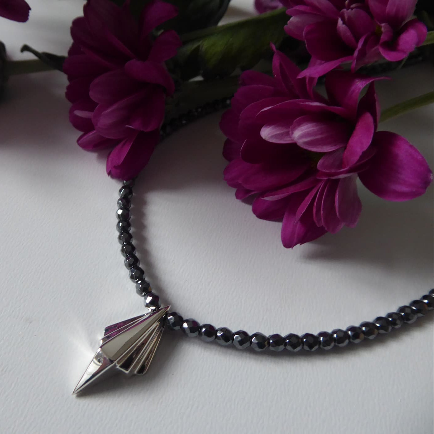 Full length Art Deco sterling silver geometric pendant on faceted hematite bead necklace, flatlay with magenta chrysanthemums