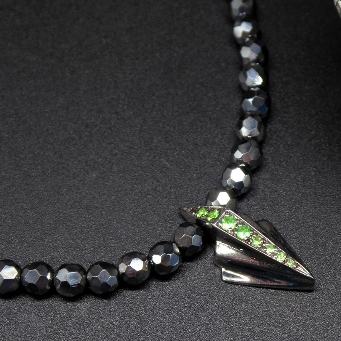 Silver Art Deco pendant with tsavorite garnets on faceted hematite bead necklace, close-up flatlay