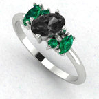 An angled perspective of the Atlantis ring, showcasing the sharp contrast of the midnight-black diamond and lush emeralds against the bright, silvery sheen of the white gold band.