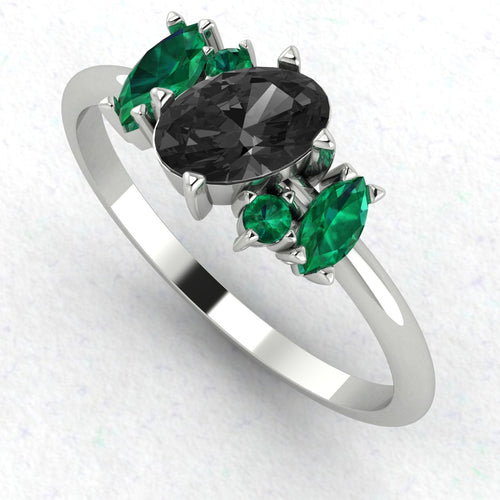 An angled perspective of the Atlantis ring, showcasing the sharp contrast of the midnight-black diamond and lush emeralds against the bright, silvery sheen of the white gold band.