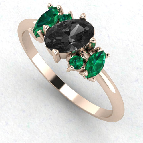 An angled perspective of the Atlantis ring, highlighting the dramatic contrast between the midnight-black diamond, lush green emeralds, and the warm tones of the handmade rose gold band.