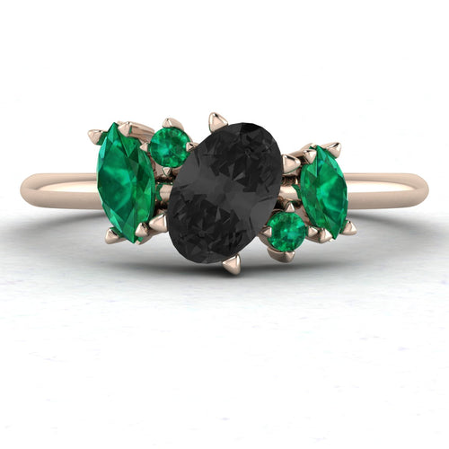 Front view of the Atlantis engagement ring, featuring a central pear-shaped black diamond surrounded by an asymmetrical cluster of vivid green emeralds and white diamonds in 18ct rose gold.