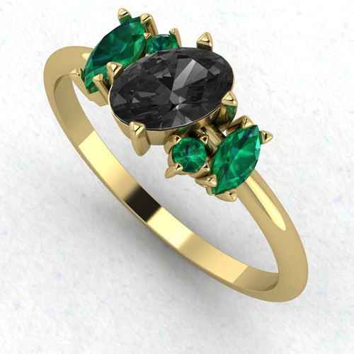 An angled perspective of the Atlantis ring, highlighting the vibrant contrast of the green emeralds and midnight-black diamond against the polished yellow gold band.