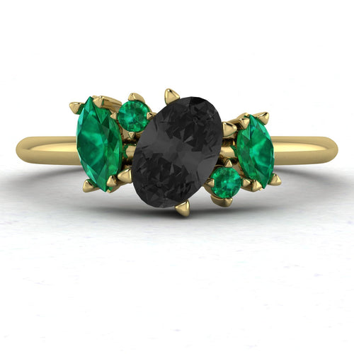 Front view of the Atlantis engagement ring in 18ct yellow gold, featuring a central pear-shaped black diamond accented by an asymmetrical cluster of green emeralds and white diamonds.
