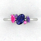 A top-down view of the Atlantis engagement ring, featuring an asymmetrical cluster of sapphires in shades of blue and teal set in white metal.