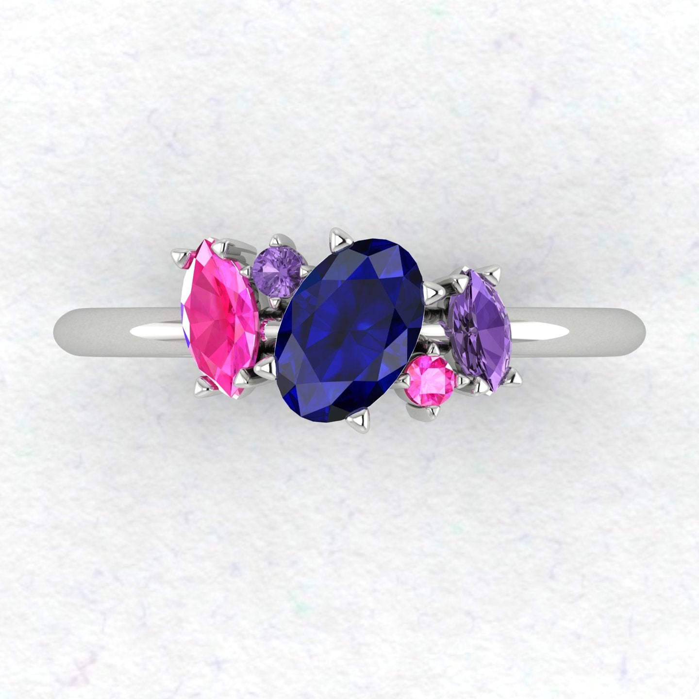 Top view of the Atlantis engagement ring featuring an asymmetrical cluster of violet, pink, and blue sapphires set in polished white metal.