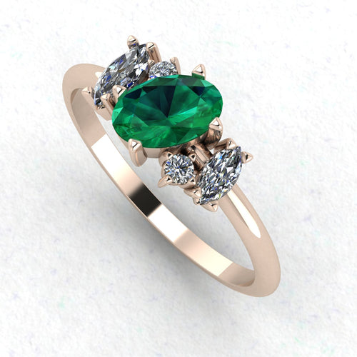 An angled perspective of the Atlantis emerald ring, showcasing the organic, handmade design and the striking contrast of lush green stones against the polished rose gold band.