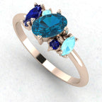 Atlantis London blue topaz and sapphire asymmetrical engagement ring in 18ct rose gold, angled view highlighting the deep blue gemstones against the warm rose gold band, handmade in our London studio