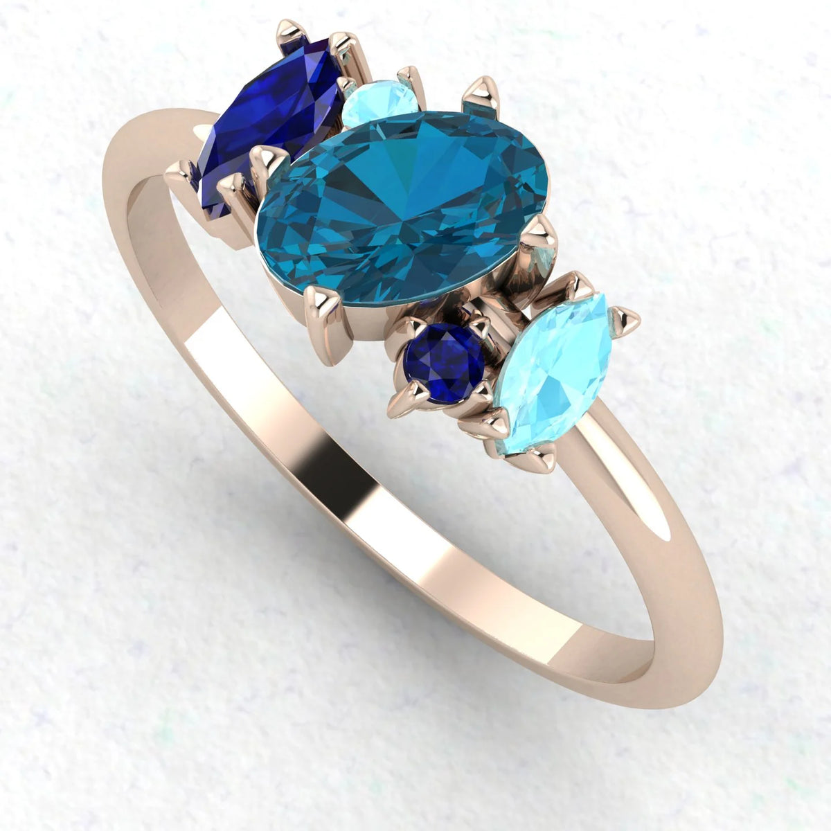 Atlantis London blue topaz and sapphire asymmetrical engagement ring in 18ct rose gold, angled view highlighting the deep blue gemstones against the warm rose gold band, handmade in our London studio