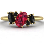 view of the Atlantis engagement ring in 18ct yellow gold, featuring a central pear-shaped black diamond surrounded by an asymmetrical cluster of crimson rubies and white diamonds.