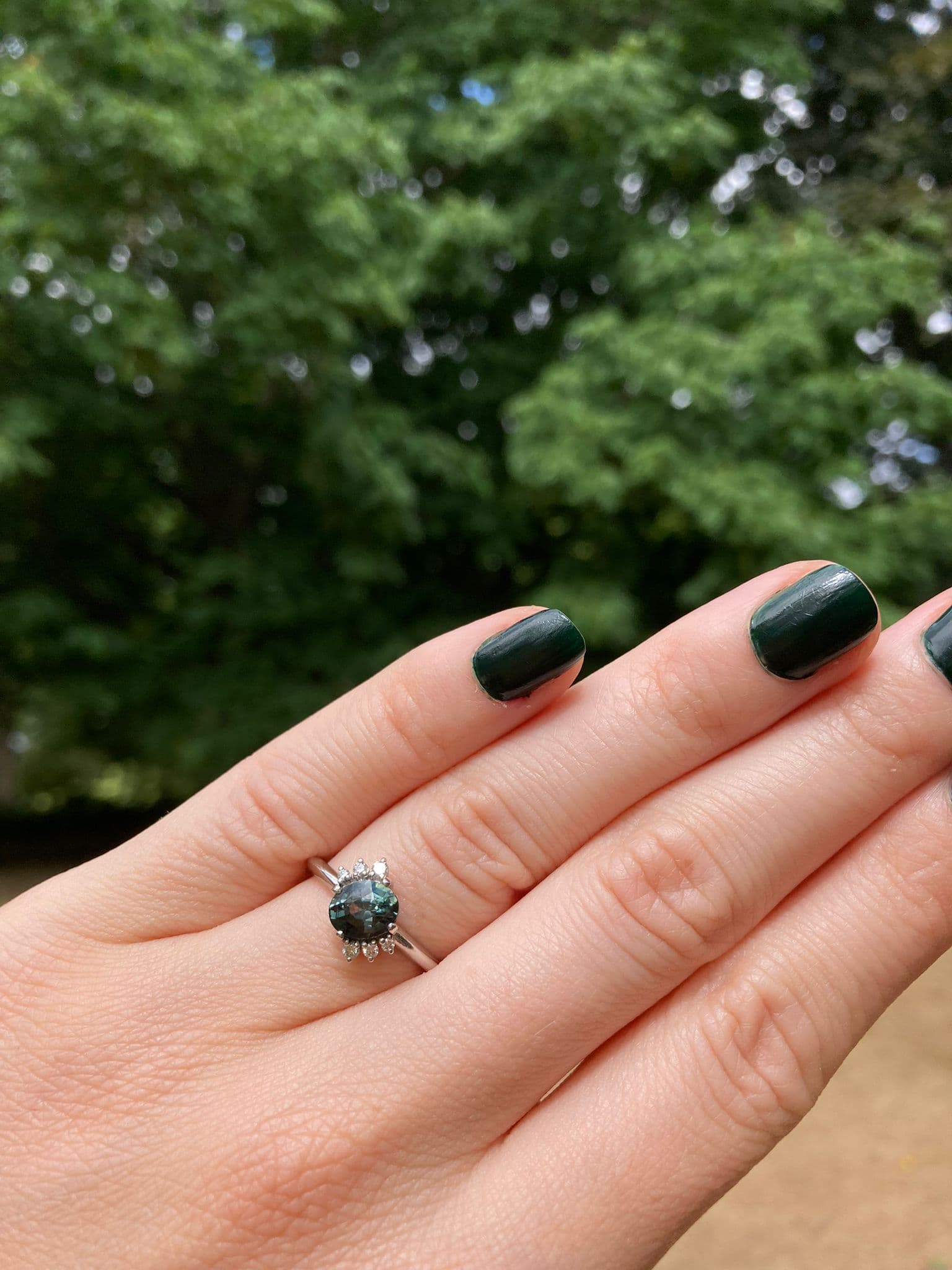 Lauren showing off her bespoke engagement ring on her hand featuring a beautiful oval teal sapphire and diamonds.