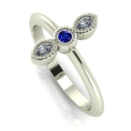 Angled perspective of an 18ct white gold trilogy ring with a sapphire and diamonds featuring fine milgrain textured edges.