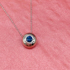 Silver necklace with a blue sapphire gemstone pendant on a pink textured background