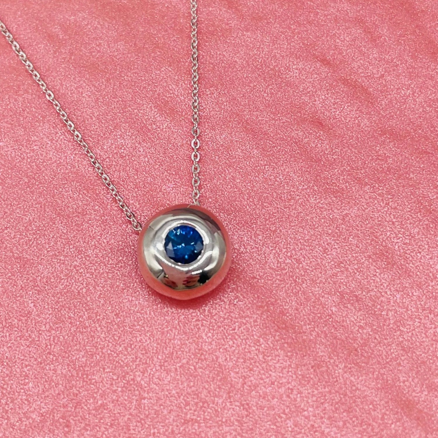 Silver necklace with a blue sapphire gemstone pendant on a pink textured background