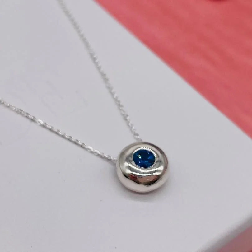 Silver necklace with a blue sapphire gemstone pendant on a white background