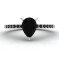 Front studio hero shot of the Calista ring, showcasing a striking pear-shaped black diamond on a band with pave-set white diamond shoulders.