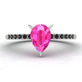 High angle studio detail shot of the Calista alternative engagement ring, showing the bright pink clarity of the sapphire facets against the dark shoulder stones.