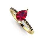 Front three-quarter studio view of the Calista ruby ring, showcasing the striking contrast of the black diamonds set into the warm, polished yellow gold shoulders.