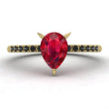 Top-down studio hero shot of the Calista engagement ring, featuring a vibrant pear-shaped red ruby on an 18ct yellow gold band with black diamond shoulders.