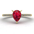 Front view of the Calista engagement ring, showcasing a vibrant pear-shaped red ruby on a polished yellow gold band with diamond shoulders.