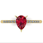 Top-down studio hero shot of the Calista engagement ring, showcasing a vibrant pear-shaped red ruby on a polished yellow gold band with diamond shoulders.