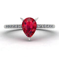 Top-down studio hero shot of the Calista engagement ring, showcasing a vibrant pear-shaped red ruby on a white gold or platinum band with diamond shoulders.