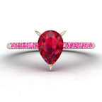 Front view studio hero shot of the Calista engagement ring, showcasing a prominent pear-shaped red ruby on a rose gold band with vibrant pink sapphire shoulders.
