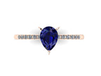 Top-down studio hero shot of the Calista engagement ring, featuring a prominent pear-shaped blue sapphire on a rose gold band with sparkling white diamond shoulders.